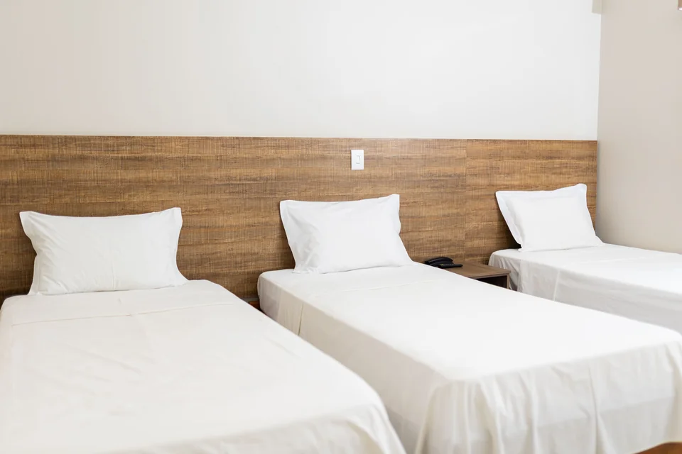 Suíte Tripla do Planalto Palace Hotel em Rurópolis, com três camas de solteiro, roupas de cama brancas e cabeceira de madeira.